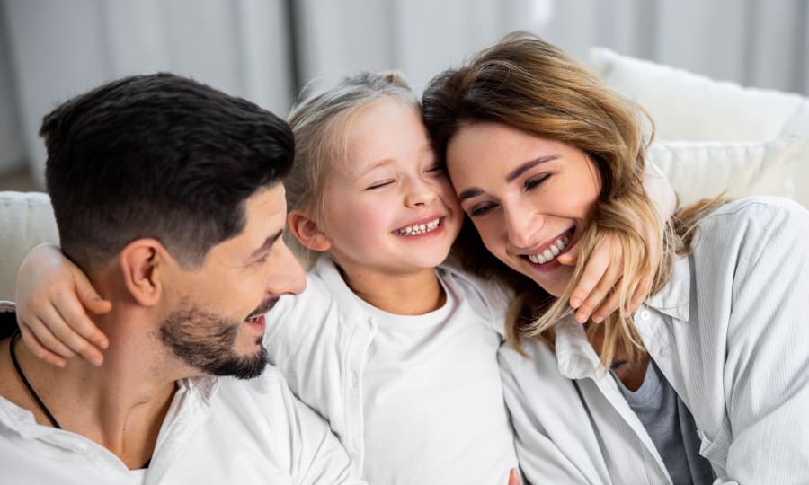 A family sits on a sofa hugging and smiling.