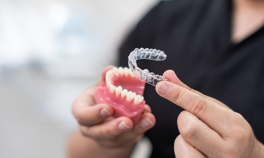 A dental professional holds an Invisalign tray over a dental model..