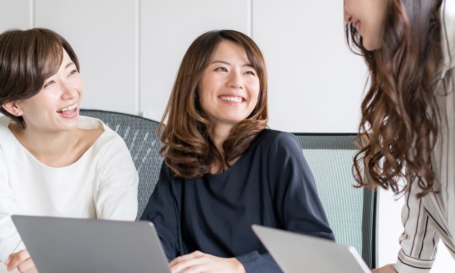A group of women sit together smiling whith laptops out in front of them.